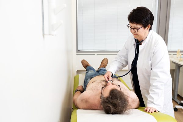 Naislääkäri kuuntelemassa stetoskoopilla hoitopedillä makaavan miesasiakkaan rintakehää.