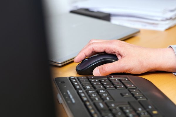 Tietokoneen näppäimistö ja tietokoneen käyttäjän käsi tietokoneen langattoman hiiren päällä, lähikuva.
